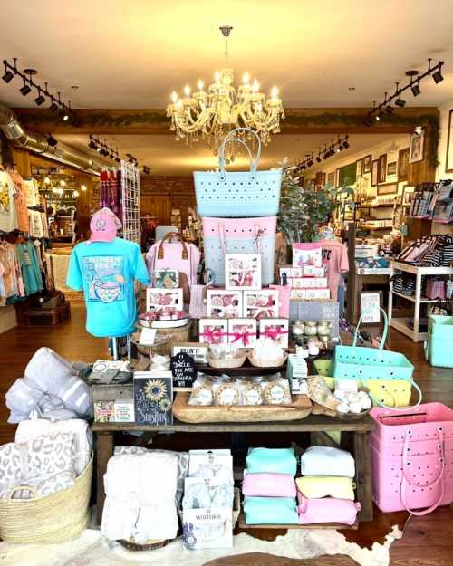 A colorful display of merchandise in a boutique, featuring bags, home decor, and clothing under a chandelier.