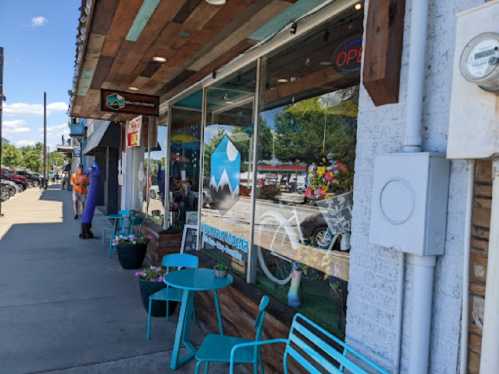 A storefront with a sign reading "Open," featuring outdoor seating and colorful decor on a sunny day.