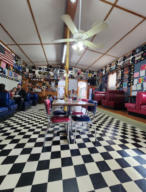 A retro diner with checkered floors, vinyl records on the walls, and colorful seating. People are seated at a table.