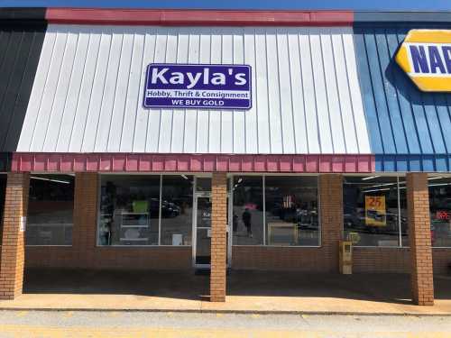 Exterior of Kayla's Hobby, Thrift & Consignment store with a sign that says "We Buy Gold." Bright, sunny day.