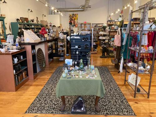 A cozy shop interior filled with various items, including crystals, jewelry, and home decor, on wooden floors.
