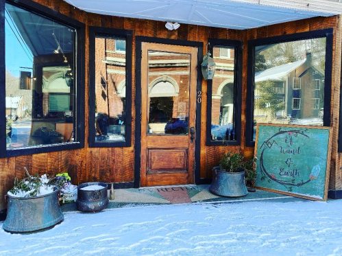 A cozy storefront with wooden siding, large windows, and a sign reading "Wizard of Earth," surrounded by snow.