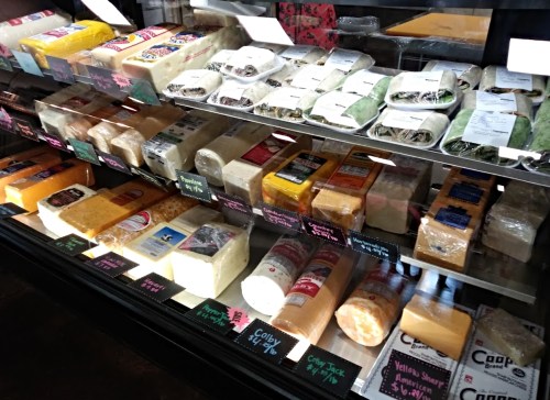 A display case filled with various types of cheese, labeled with colorful tags, showcasing a variety of textures and colors.