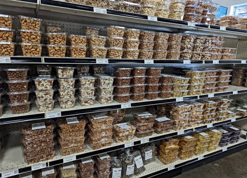 A grocery store shelf filled with various containers of nuts and dried fruits, neatly organized in rows.