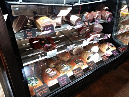 A display case filled with various deli meats and cheeses, labeled with prices on small signs.