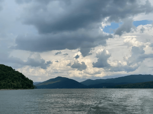 A serene lake surrounded by green hills and mountains under a cloudy sky.
