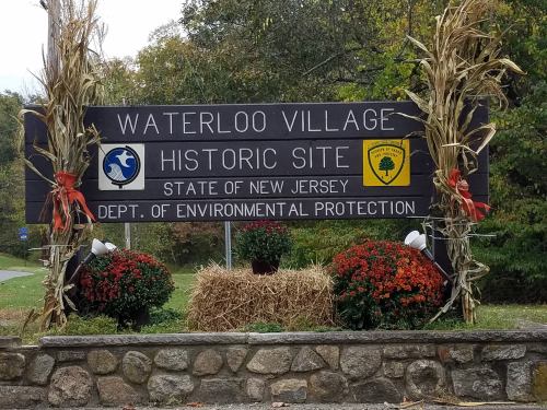 Sign for Waterloo Village Historic Site in New Jersey, featuring decorative plants and environmental protection logos.