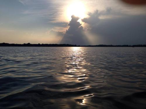 A serene lake at sunset, with shimmering water reflecting the sun and clouds in the sky.