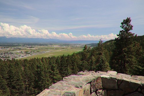 A panoramic view of a valley surrounded by mountains, with lush trees in the foreground and clouds in the sky.