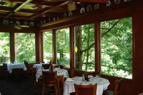 A cozy restaurant interior with wooden decor, tables set for dining, and large windows overlooking lush greenery.