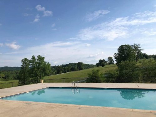 A serene outdoor pool surrounded by green hills and trees under a partly cloudy sky.