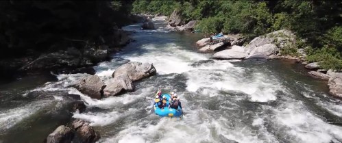 A group of people in a blue raft navigating through a rocky river with rapids and lush greenery surrounding the area.
