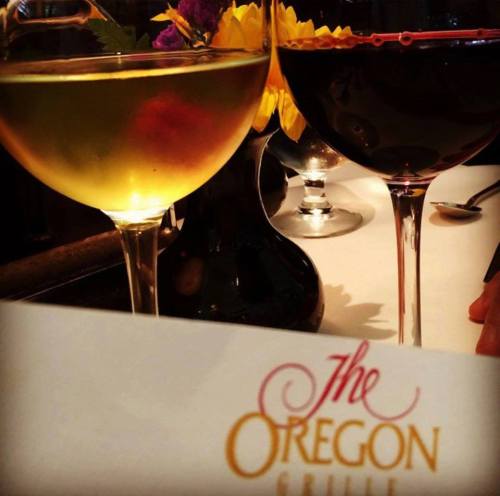 Two glasses of wine, one white and one red, with a menu from The Oregon Grille and colorful flowers in the background.
