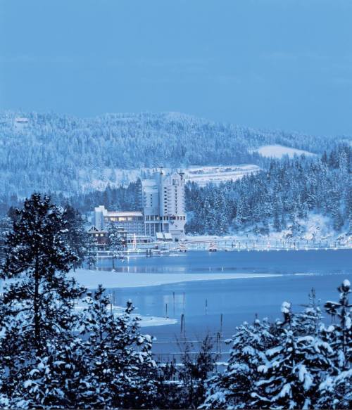 A snowy landscape featuring a lake, trees, and a distant building surrounded by hills.