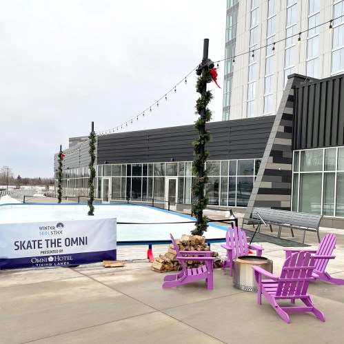 Outdoor ice skating rink with festive decorations, surrounded by purple chairs and a modern hotel building in the background.