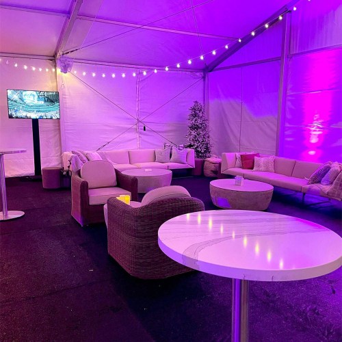 A cozy event space with purple lighting, lounge seating, and a small table, decorated for a festive atmosphere.