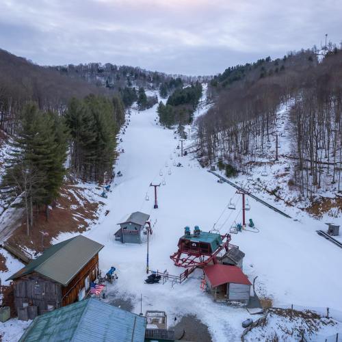 A snowy ski slope with a chairlift, surrounded by trees and a rustic building in the foreground.