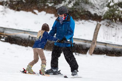 A child and an adult are skiing together in a snowy landscape, with snowflakes falling around them.