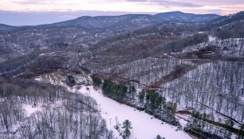 Aerial view of a snow-covered landscape with rolling hills, bare trees, and a winding river in a serene winter setting.