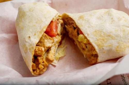 A close-up of a halved burrito filled with chicken, lettuce, and tomato, wrapped in a tortilla.