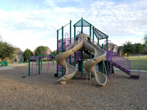 A playground with a large slide, climbing structures, and purple and green equipment on a gravel surface.