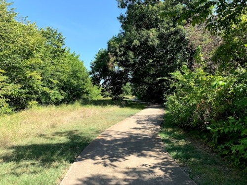 A paved path winds through lush greenery under a clear blue sky.