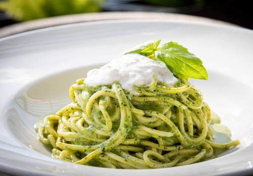 A plate of spaghetti topped with creamy pesto sauce and a dollop of ricotta, garnished with a fresh basil leaf.