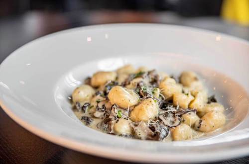 A plate of creamy gnocchi with mushrooms and herbs, garnished with cheese, served in a white bowl.