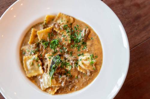 A bowl of ravioli in a creamy sauce, garnished with fresh herbs, served on a wooden table.