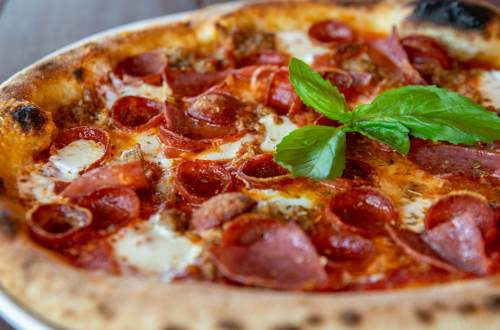 A close-up of a pepperoni pizza topped with mozzarella cheese and fresh basil leaves.