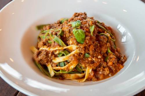 A bowl of fettuccine pasta topped with a rich meat sauce and garnished with fresh basil.