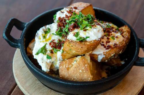 A cast iron dish filled with toasted bread topped with creamy cheese, herbs, and crispy bits, garnished with fresh parsley.