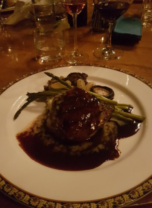 A gourmet dish featuring a seared steak with sauce, asparagus, and mushrooms on a decorative plate.