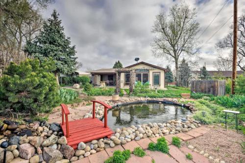 A serene garden with a pond, red bridge, and lush greenery, featuring a house in the background under a cloudy sky.