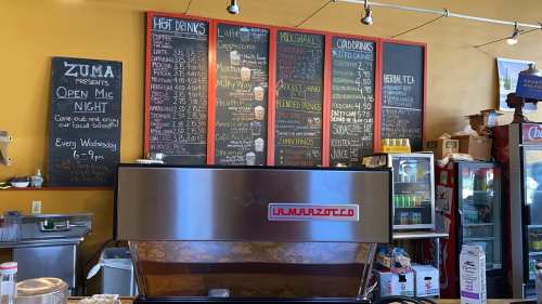 A coffee shop interior featuring a menu board with drinks and snacks, and a coffee machine in the foreground.