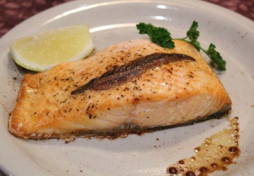 A cooked salmon fillet garnished with a slice of lemon and a sprig of parsley on a white plate.