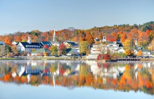 A serene lakeside view with colorful autumn trees reflecting on the water and charming buildings in the background.