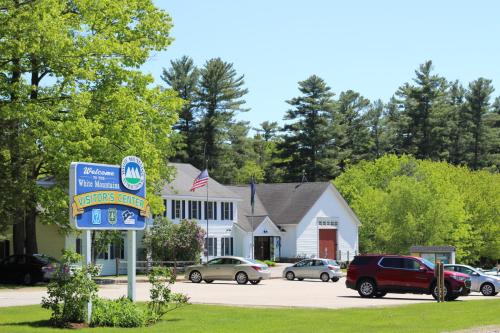 A visitors center in a green area, featuring a welcome sign, cars parked, and trees in the background.