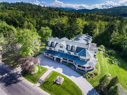 Aerial view of a large, multi-roofed building surrounded by lush greenery and mountains in the background.