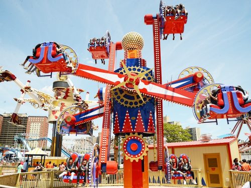 A colorful amusement park ride with spinning seats and excited riders against a clear blue sky.