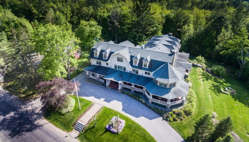 Aerial view of a large, multi-story house surrounded by trees and a landscaped yard.