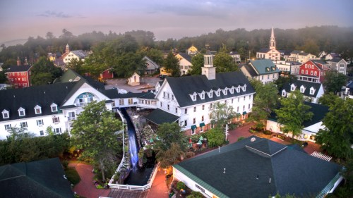 Aerial view of a charming village with colorful buildings, lush trees, and a misty backdrop.