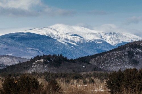 Snow-capped mountains rise above a forested landscape under a clear blue sky.