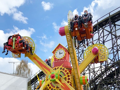 Two people enjoy a colorful amusement park ride with a large clock and gears, set against a blue sky.