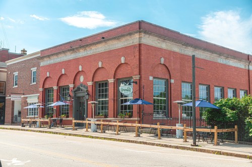 A brick building with large windows and outdoor seating under umbrellas, featuring a sign that reads "Grandly."