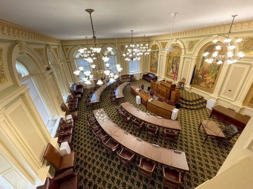 Aerial view of a grand legislative chamber with ornate decor, long tables, and chandeliers.