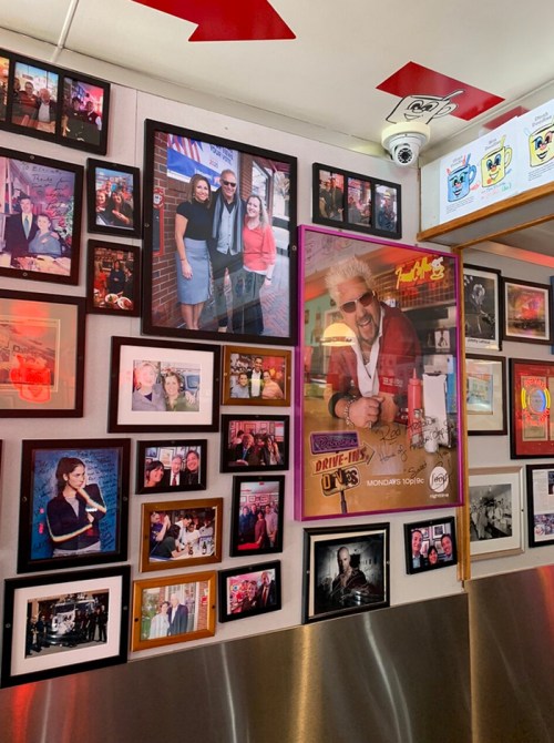 A wall covered with framed photos, including celebrity portraits and candid shots, in a vibrant restaurant setting.