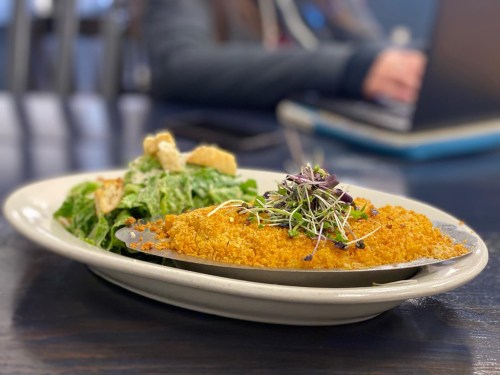 A plate with a baked dish topped with breadcrumbs and microgreens, alongside a fresh salad with croutons.