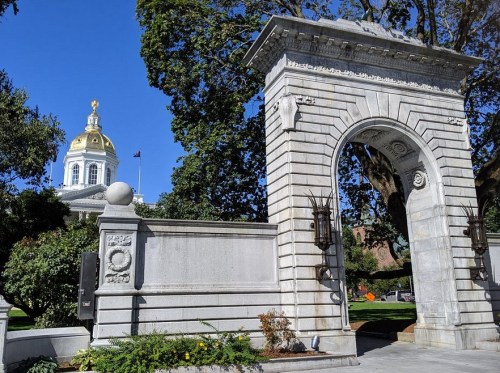 A stone archway with decorative elements, leading to a park, with a gold-domed building visible in the background.