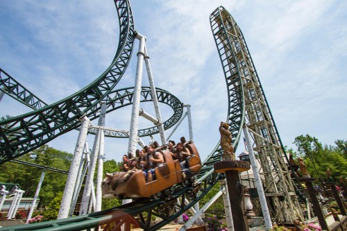 A roller coaster with a twisting track and riders enjoying the thrill on a sunny day at an amusement park.
